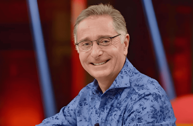 Paolo Bonolis sorridente in studio televisivo con capelli grigi ben curati